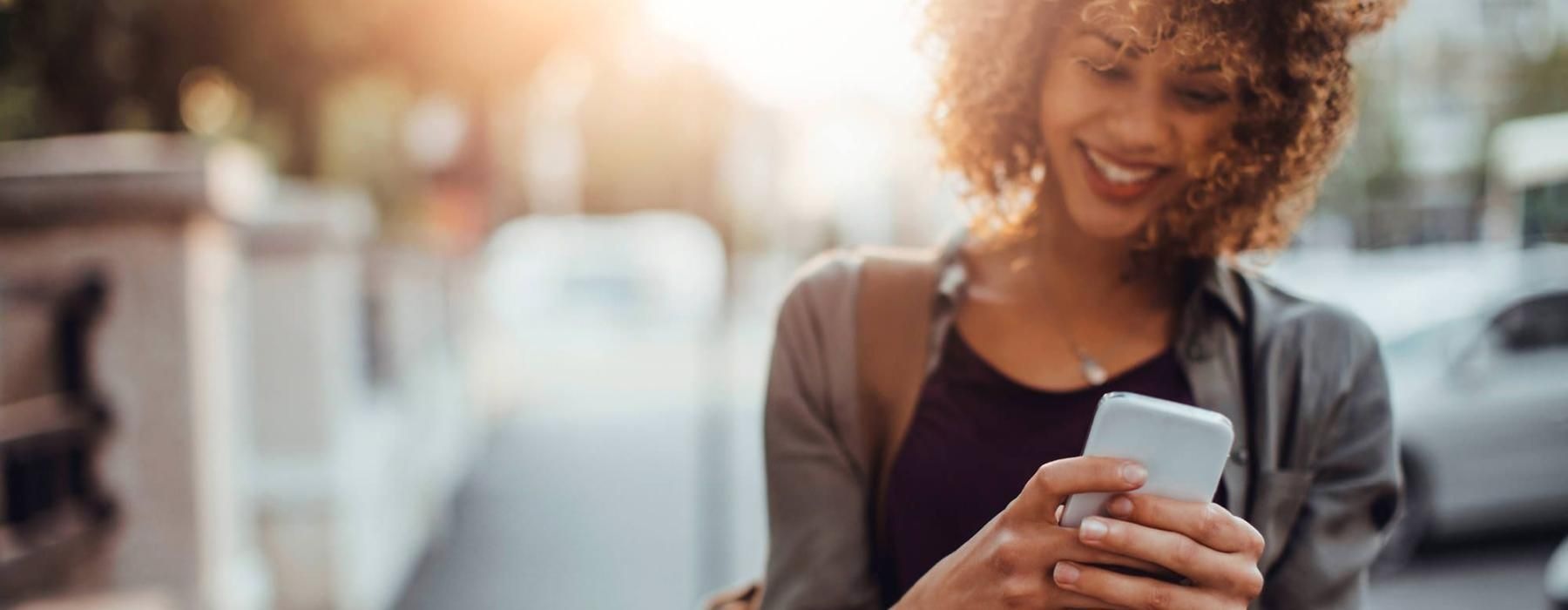 woman texts on her phone as she walks through the city